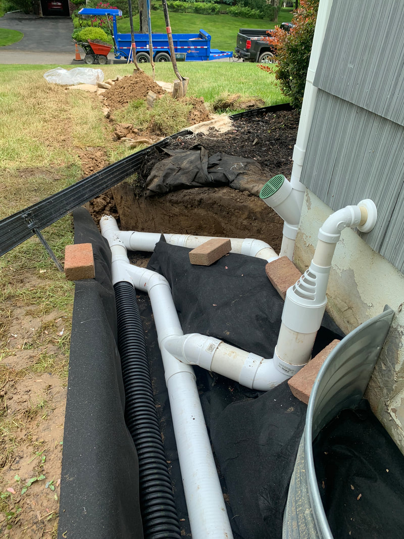 DIY drainage ideas for the exterior of a house, landscape, and yard. How to install underground drainage outside a home picture. Drainage solution to fix an outdoor water problem. Home improvement project idea for exterior basement waterproofing, landscaping, plumbing, and drainage systems. 